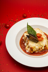 Lasagna with mussels and tomato sauce on a red background