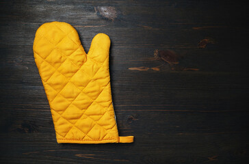 Yellow cooking glove on wood table background. Kitchen utensil. Space for text. Flat lay.