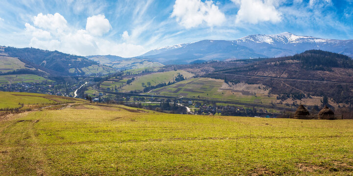 carpathian countryside landscape in spring. rural field with arable and forest on the hill. road winding through village in the distant valley. snow capped mountain peak beneath a blue sky with cloud