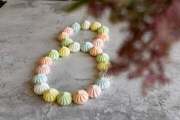 International Women's Day, a holiday for girls, the eighth of March, on the table are sweet colored bize cakes in the form of a number eight, and flowers on a light background, symbolic decorations 