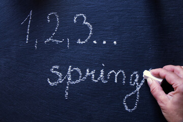 Bird eye picture of a woman hand writing with chalk on a black stone slate countdown for spring