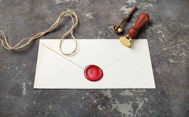 Blank vintage envelope with wax seal, stamp, spoon and rope on concrete background.