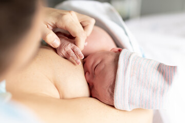 mom breastfeeding her newborn baby in the hospital while holding the fingers of her little hand