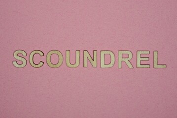 text the word scoundrel from gray wooden small letters on an pink table