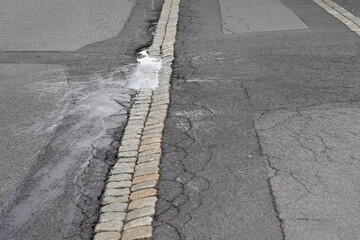 Pothole on a sidewalk and road. The pothole is full of rainwater. Around there are splashes of...