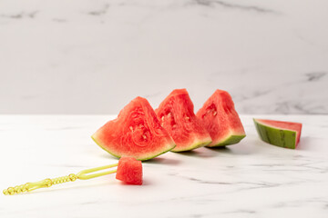 A ripe watermelon is cut into triangular segments lying on a plate. Disposable food plug