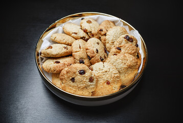 Dish with homemade oatmeal cookies on black table.