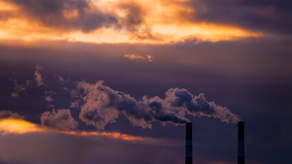 Industrial chimneys with heavy smoke causing air pollution on the beautiful orange sky with violet clouds, nature sunset