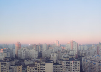 Fototapeta na wymiar Cute, pink sky without clouds at sunrise over morning city. Clear heaven background is pastel, subtle and gentle. Town in aerial perspective at evening, sunset.