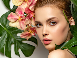 Beautiful woman with green leave near face and body. Closeup girl's face with green leave. Pretty girl in Skin care beauty treatments concept. Model with pink tropical orchid near face. Brown makeup.