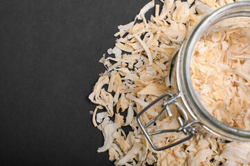 dried chopped onion in a jar and scattered next to the jar on a black background