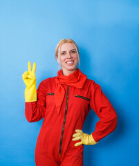 A cleaner in a red uniform with yellow gloves is happy and smiling and shows a V sign.