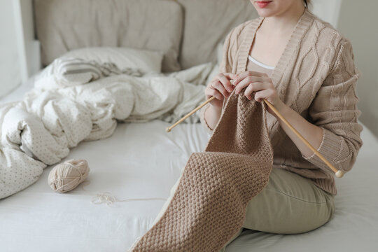 Women's hands knitting from woolen beige yarn.