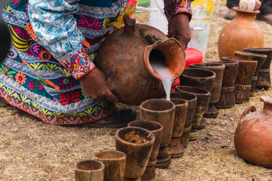 ceramic pot of traditional chicha de jora and wooden glasses in a traditional ritual on a sunny day