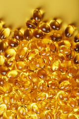 Heap of transparent fish oil capsules on yellow background with free space