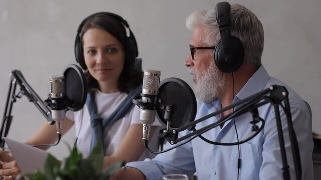 man and a woman record a podcast or interview with a microphone in a recording studio. an adult gray-haired man and a young European woman create audio content, record ads and audio books. adult