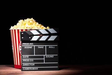 Cinema concept. Popcorn in a box and movie clapper on wooden table under beam of light against...