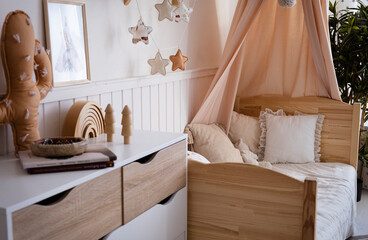 Fototapeta na wymiar Canopied cradle between gold armchair and basket with teddy bear in pink baby's bedroom
