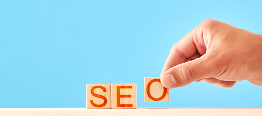 seo - search engine optimization, a man stacks wooden blocks on a blue background into an inscription.