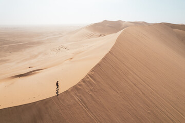 Aerial wide shot off man walking on top of sand dunes