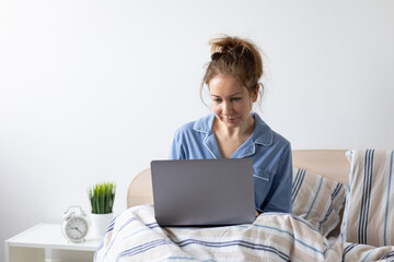 Young woman working in her pyjama from home from her bedroom in the morning. Checking mails, making conference calls, shopping online. Copy space for text