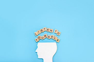 Silhouette of human and the words listen to yourself on wooden blocks with letters on blue...