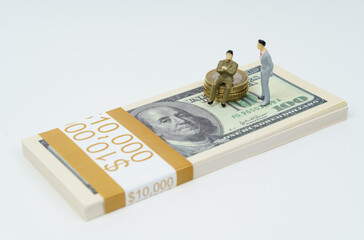 On a white surface lies a pack of dollars, on which stands a figure of a businessman, next to the...