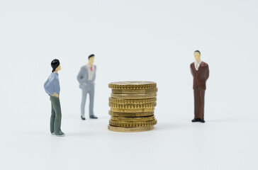 Coins lie on a white surface, miniature figures of businessmen stand nearby - they look at the coins