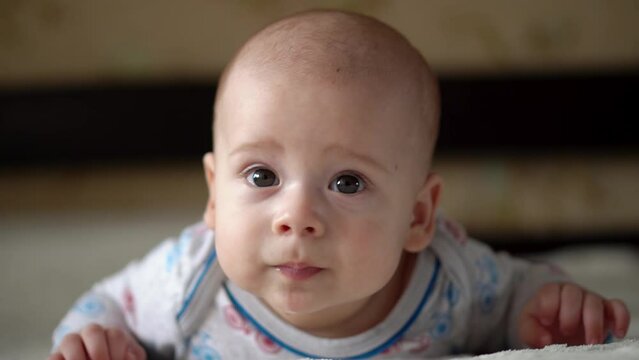Newborn Active Baby Cute Smiling Teethless Face Portrait Early Days On Stomach Developing Neck Control. 5 Months Child On White Bed Looking on Camera. Infant, Childbirth, Parenthood, Beginning Concept