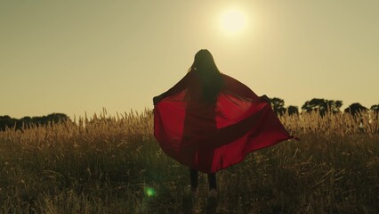 happy girl play superheroes they run across green field in red cloak, cloak flutters in wind....