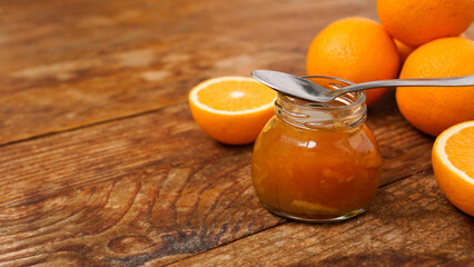 Jar of orange jam and a metal spoon on wooden background from top view. Place for text. Homemade orange marmalade, confiture in thick syrup.