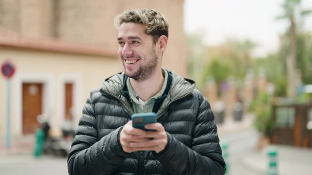 Young man smiling confident using smartphone at street