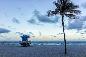 Atlantic ocean in Hollywood Beach, North Miami, Florida stormy summer weather waves at dawn sunrise with blue hour sky in morning, palm tree and lifeguard hut building and nobody