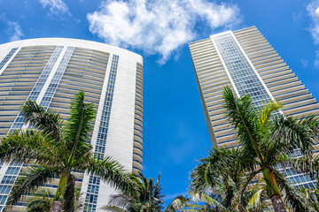 Fototapeta na wymiar Miami apartment condo buildings in Hallandale Beach, Florida with palm trees on sunny day blue sky looking up low angle view of cityscape