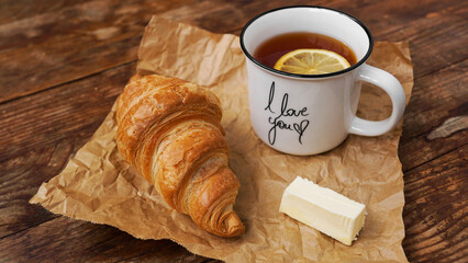 Fresh croissants with butter and a cup of tea with lemon on a wooden table. Top view. Ingredients for delicious breakfast