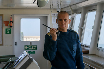Deck officer on navigational bridge with portable VHF radio. Walkie-talkie. Commercial shipping. Passenger ship.