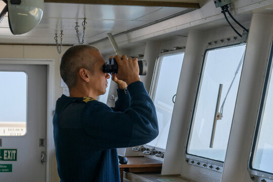 Deck officer with binoculars on navigational bridge. Seaman on board of vessel. Commercial shipping. Passenger ship.