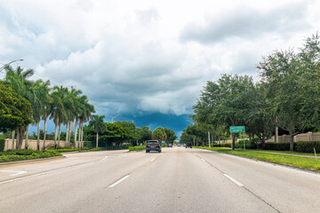 Fototapeta na wymiar Naples, USA Airport-Pulling open empty road street with cars in traffic on cloudy stormy day with sign driving point of view