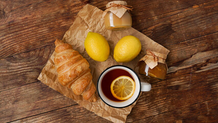 Lemon tea, home made jam, marmalade or curd, croissant on wooden table. Breakfast concept. Top view.