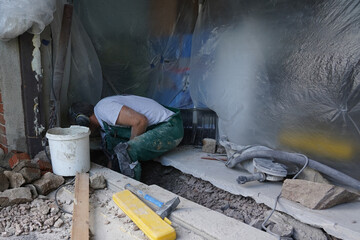 A man in green trousers and white t-skirt filling up bucket with crushed stones.