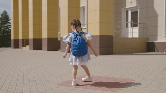 Little child with school backpack having fun spin in school yard, happy dreamy kid, first grader loves to play dizzying games, fun game for childhood, education and development preschool age outdoors