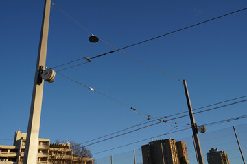 View on automatic tensioning system for rail and tramway which use force of a coil spring to keep constant tension on railway catenary and bearer cable installed on poles. Buildings are in background.