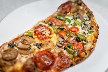 Half a small homemade pizza closeup on white plate with melted mozzarella cheese, red tomato sauce, pepperoni vegetable toppings and green peppers