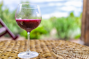 Naklejka premium Glass of dark red purple wine or cranberry juice on wicker table in Santa Fe desert garden backyard with closeup of one drink and bokeh background of scenery