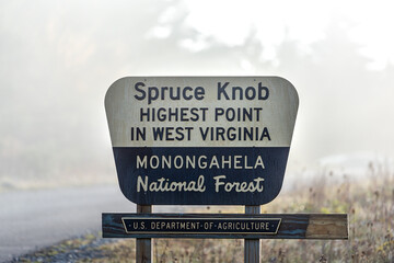 Sign closeup at Spruce Knob West Virginia mist fog autumn fall season by empty road for highest...
