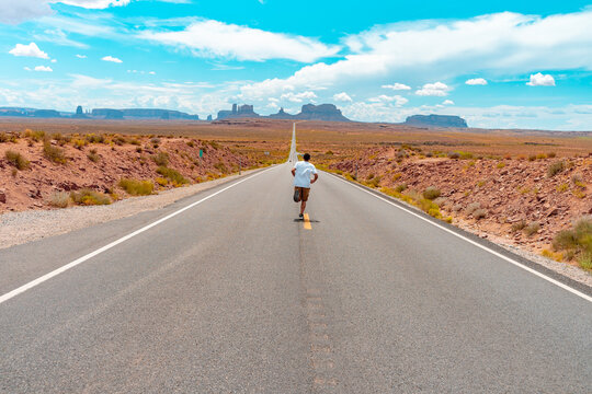 Attractive young man from back view running in the middle of American straight road in the desert.