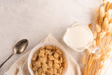 On a white background, a bowl with whole grain pads, milk in a jug, a spoon and a bunch of cereals. There is an empty space to insert. Express breakfasts, healthy lifestyle.