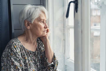 portrait of a sad grandma sitting all alone during Mother's Day and looking out of the window. High quality photo