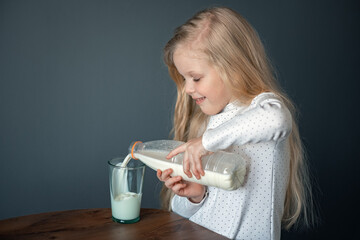 Little girl pours milk into a glass