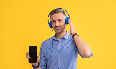 smiling mature man listen music in headphones showing phone, mobile technology